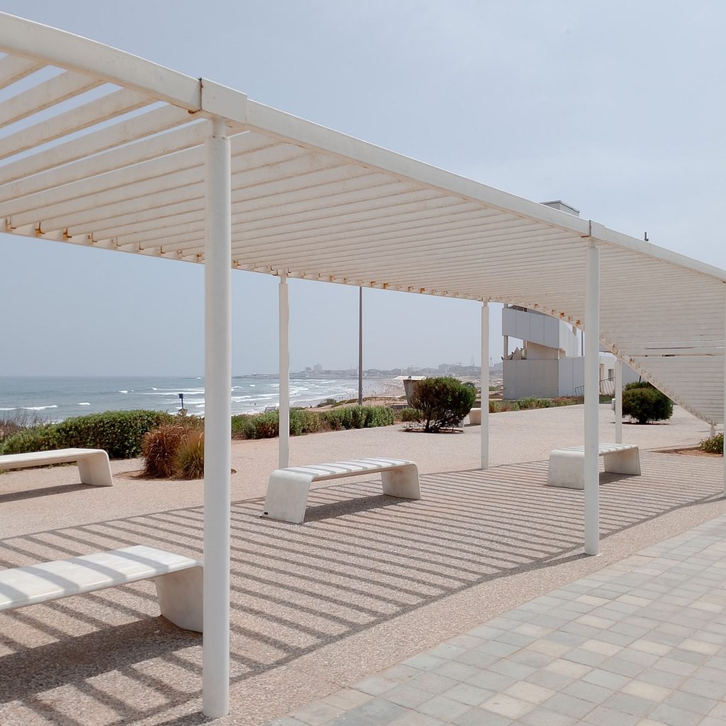 Installation publique contenant une pergola métallique blanche et des bancs en acier