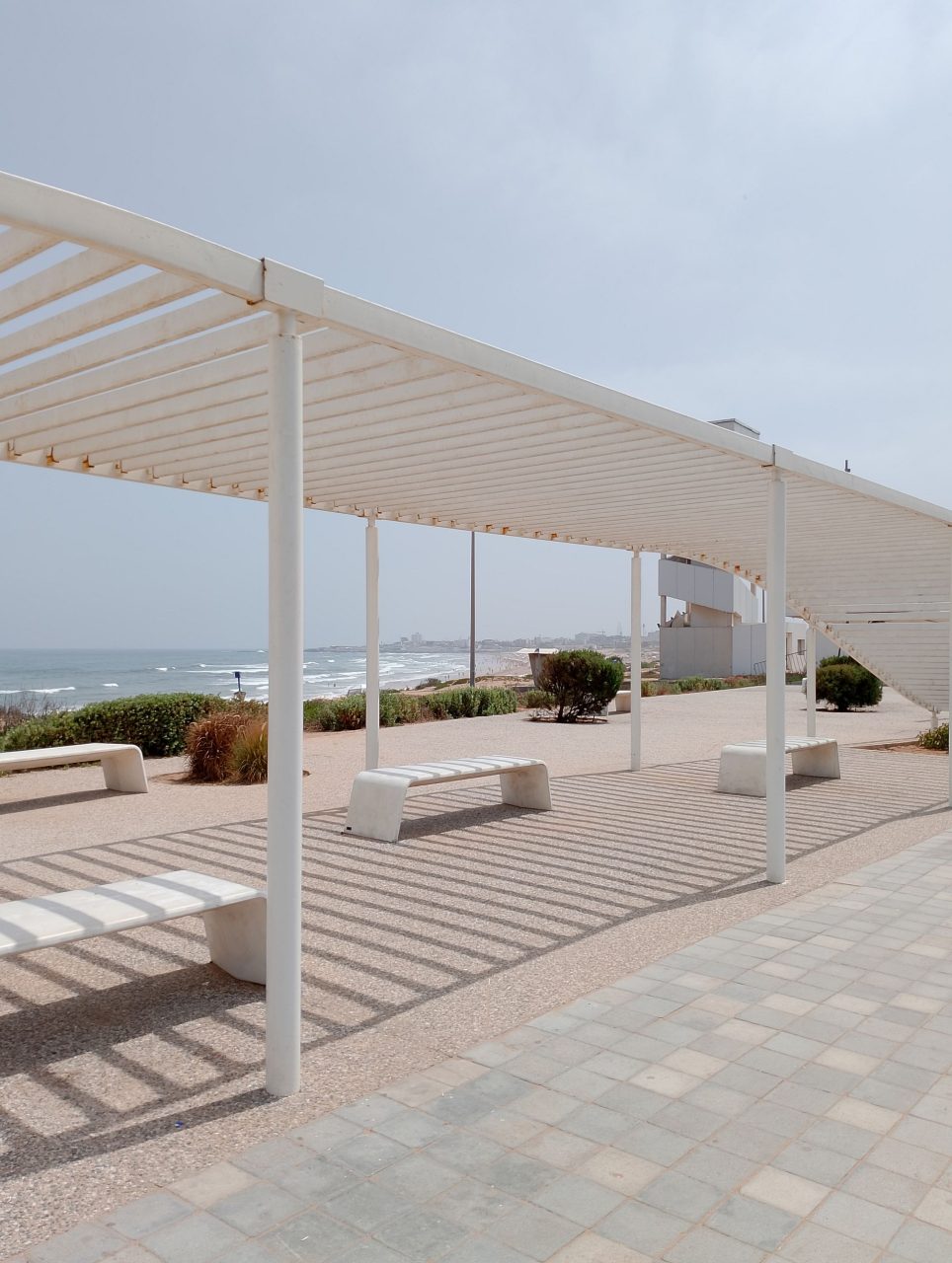Installation publique contenant une pergola métallique blanche et des bancs en acier