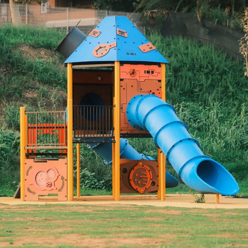 Aire de jeux située dans un parc avec un toboggan métallique bleu