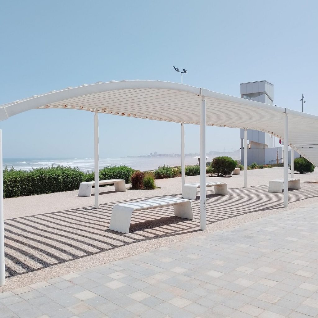 Structure métallique blanche avec des bancs situés sur une rue piétonne au bord de la mer