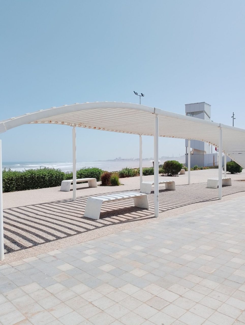 Structure métallique blanche avec des bancs situés sur une rue piétonne au bord de la mer